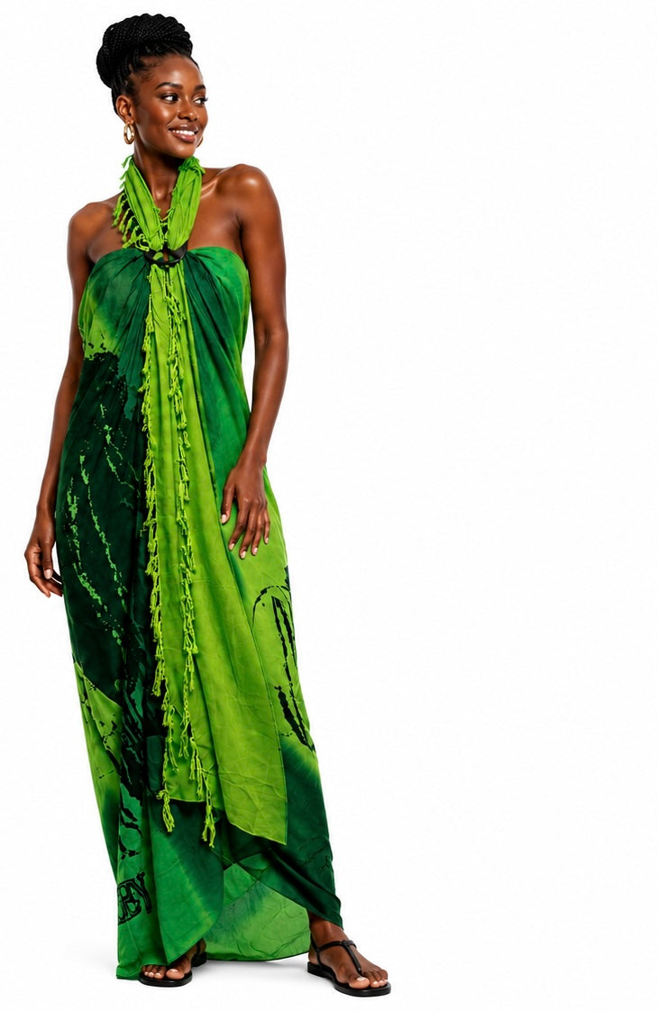 A woman modeling a green halter-neck maxi dress with a tie-dye pattern and tassel fringe, set against a plain white background.