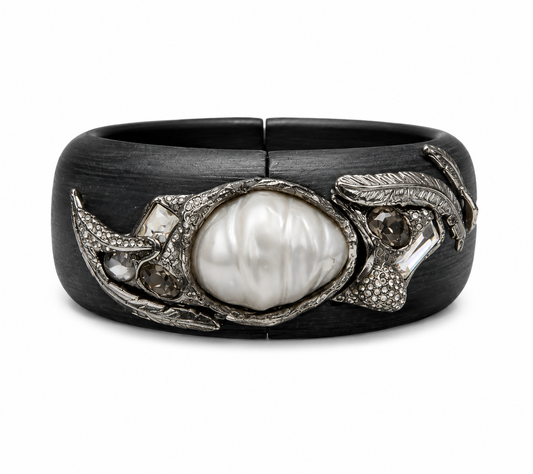 A wide black cuff bracelet featuring a central white pearl surrounded by textured silver-toned metal and small clear stones, shown on a plain white background.