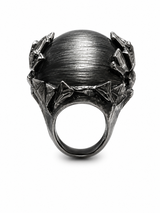 A dark gunmetal gray ring featuring a large, textured spherical top flanked by sculpted, leaf-like side details, shown on a plain white background.