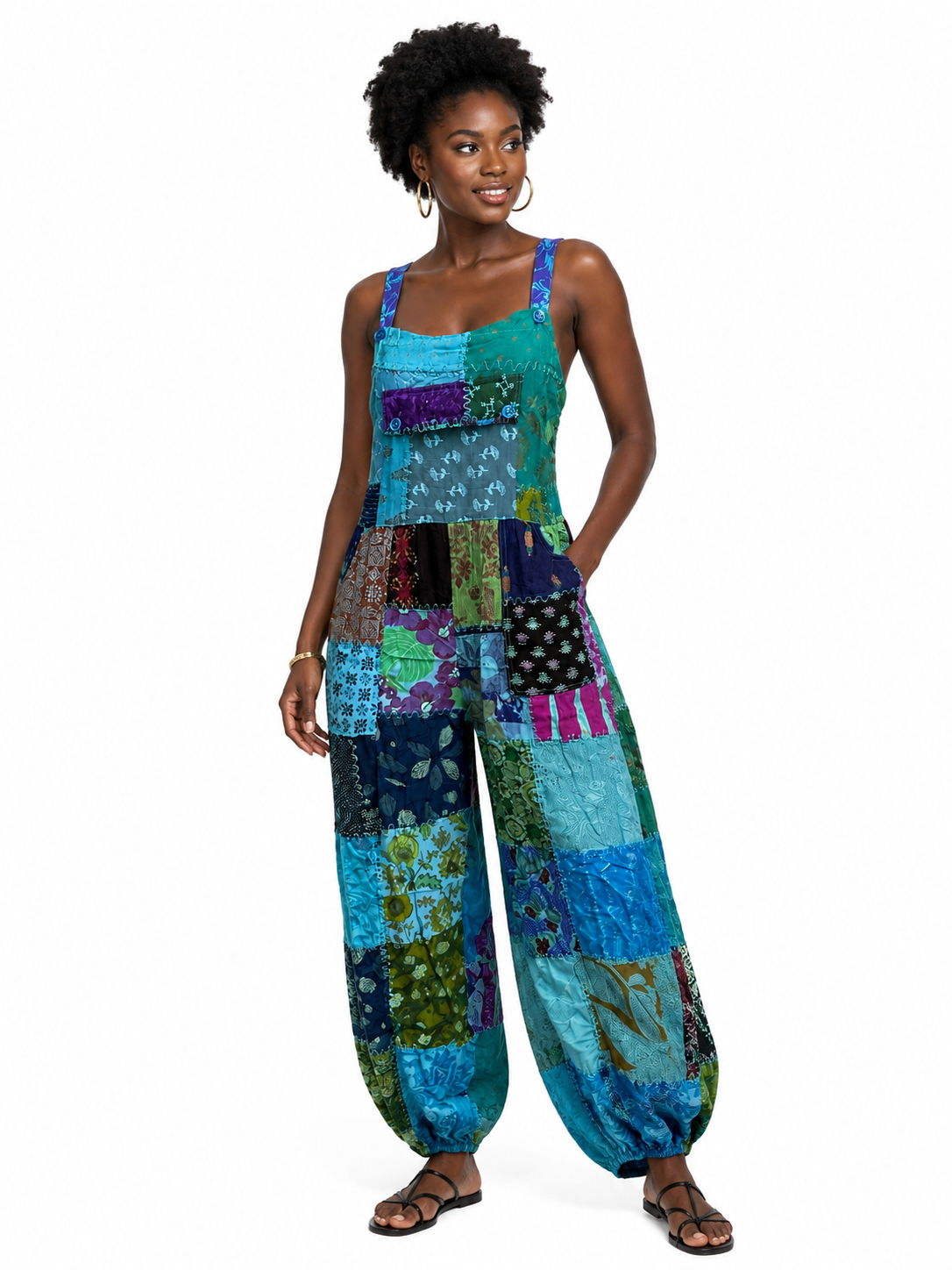 A woman modeling a sleeveless patchwork harem jumpsuit with vibrant blue, green, purple, and black patterned fabric panels, set against a plain white background.