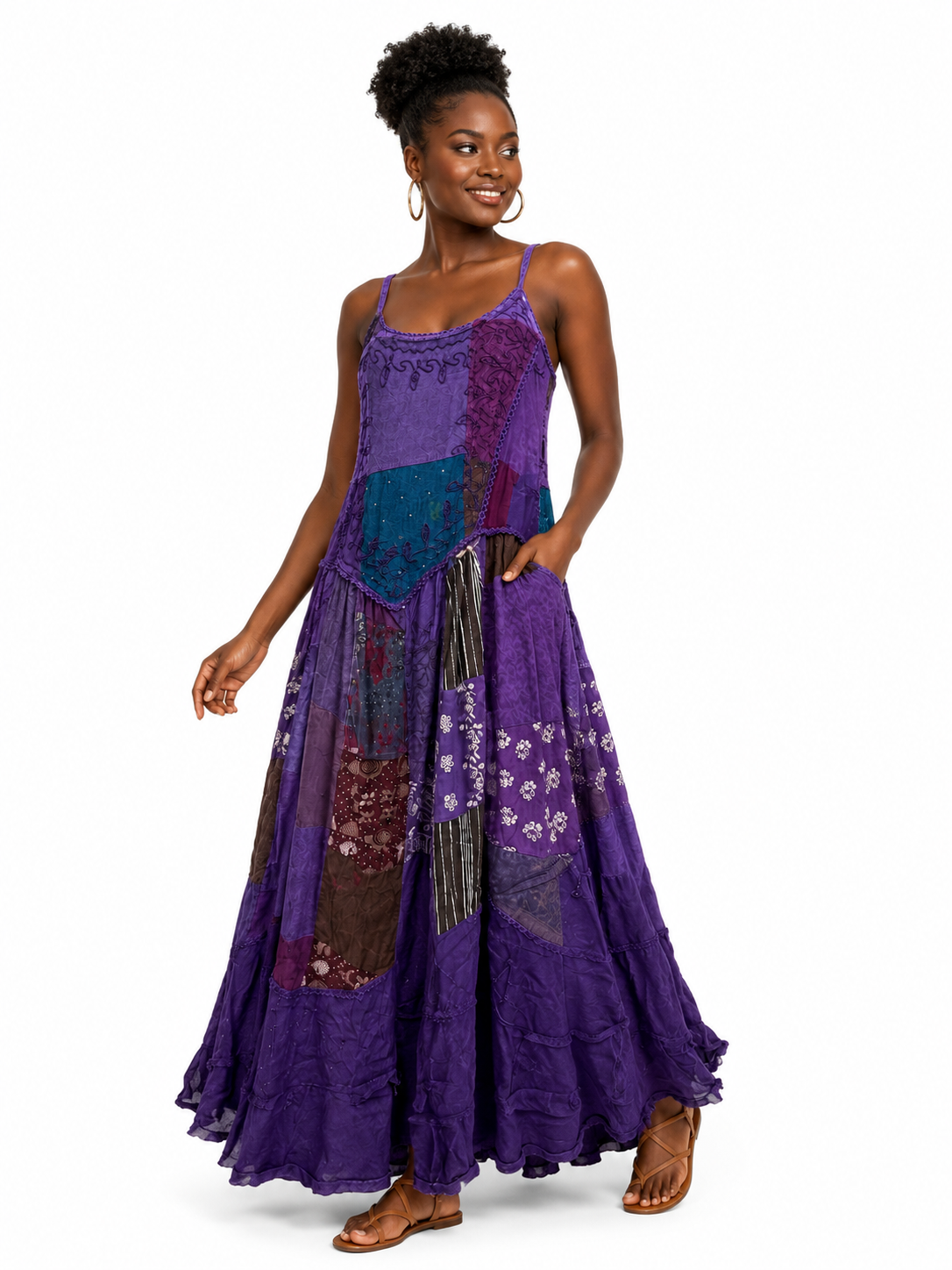 A woman modeling a sleeveless, patchwork-style maxi dress in shades of purple, teal, and brown, featuring floral prints and lace-like panels, set against a plain white background.