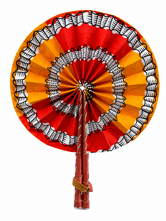 A traditional African hand fan with concentric rings of red, orange, and yellow patterned fabric, featuring black and white geometric designs, on a solid white background.